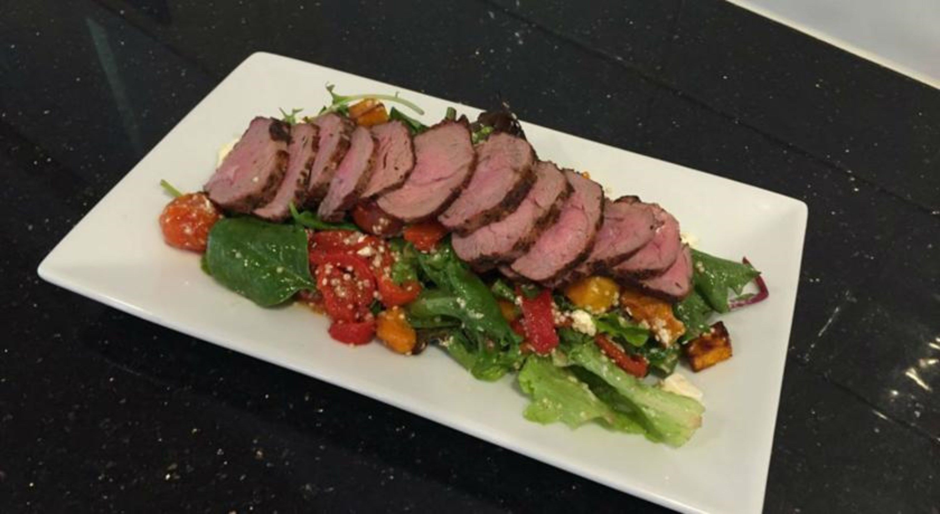 A rectangular white plate with sliced meat and a salad.