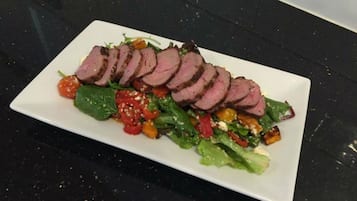 A rectangular white plate with sliced meat and a salad.