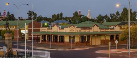 A motel with a green roof, a statue in front, and a clock tower in the background.