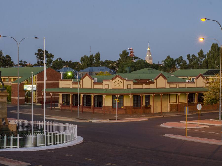 Un motel con techo verde, una estatua al frente y una torre de reloj en el fondo.