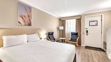 A hotel room with a large bed, two chairs, a small table, and a door with a sign.
