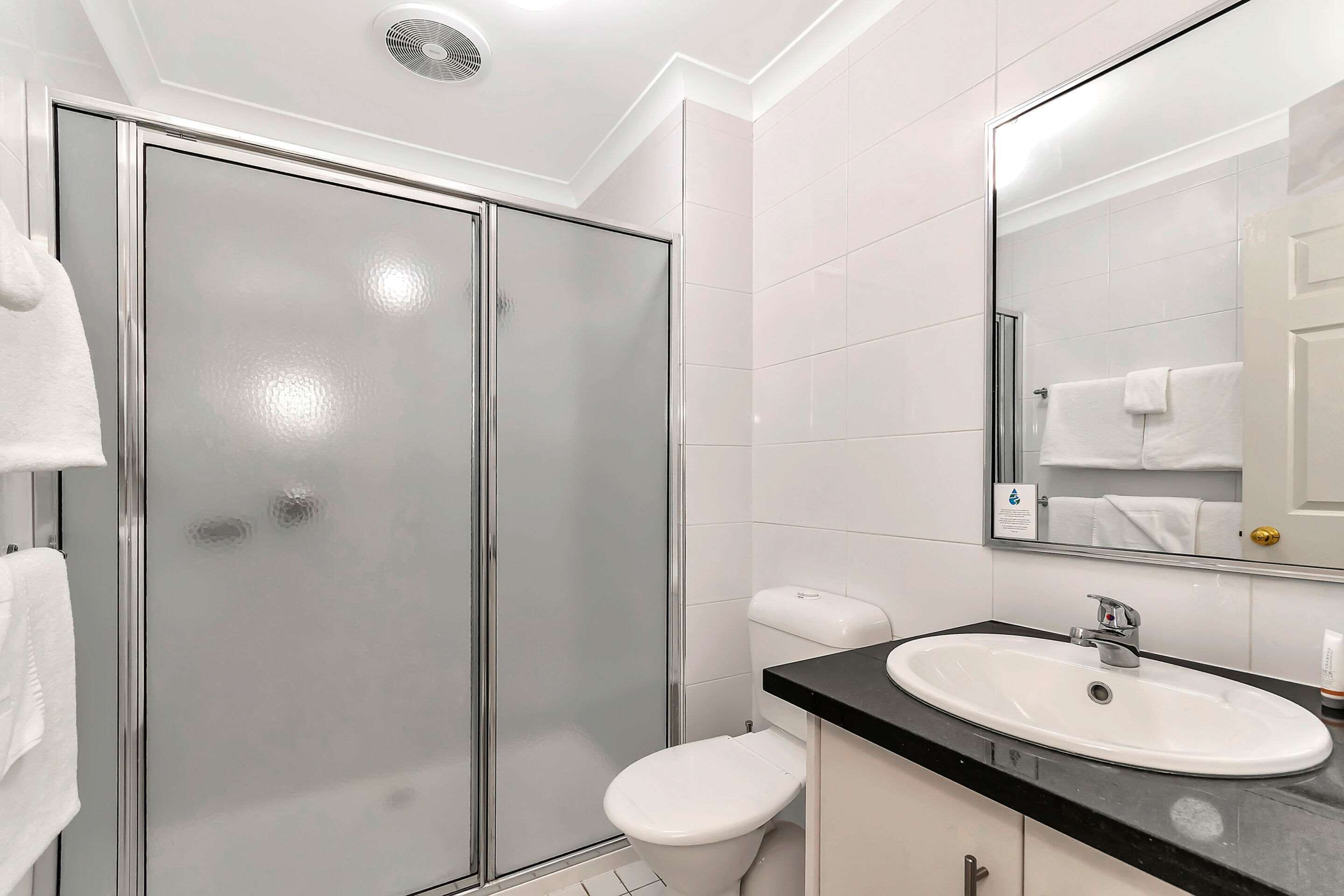 A modern bathroom with a glass-enclosed shower, a white toilet, and a black countertop sink.