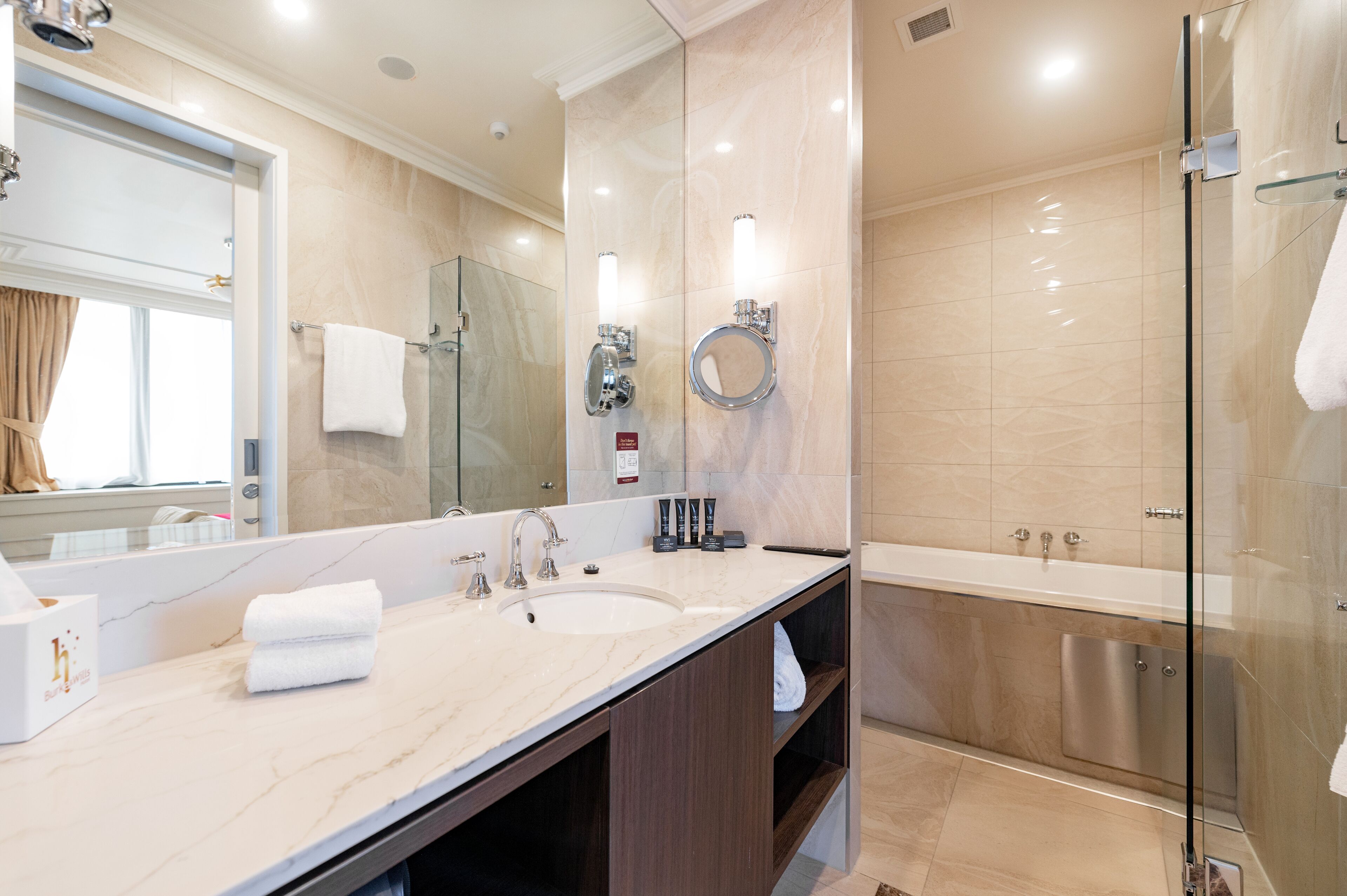 A modern bathroom with a large mirror, two sinks, a glass shower enclosure, and a bathtub.