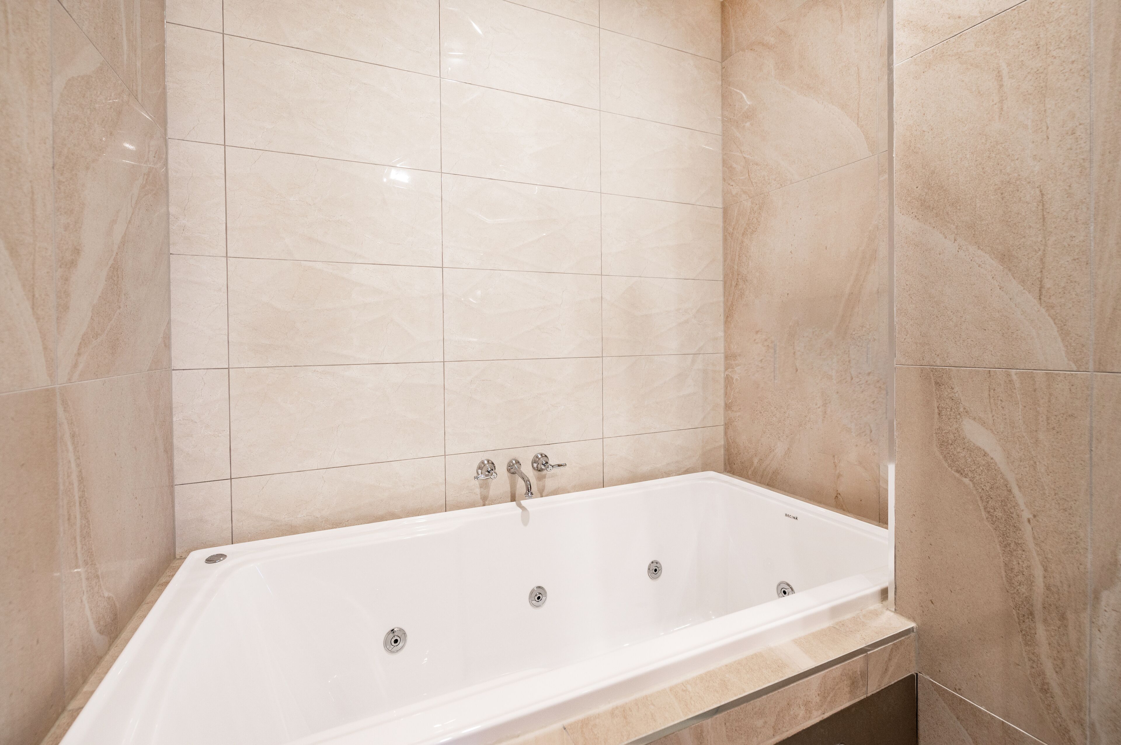 Een moderne badkamer met een vrijstaand bad, betegelde wanden en een vloer van marmerlook.