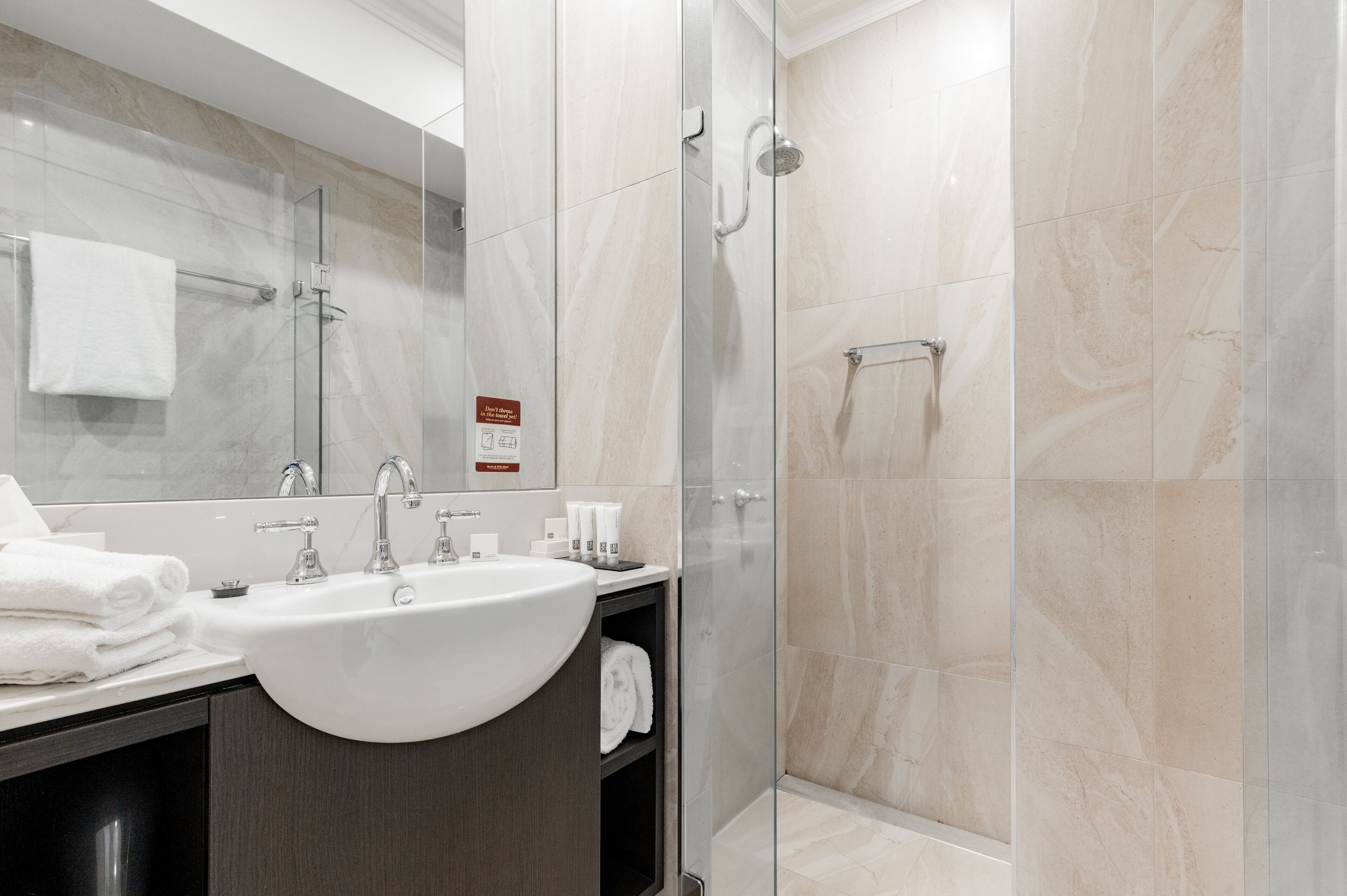 A modern bathroom with a large sink, mirror, and glass shower enclosure.