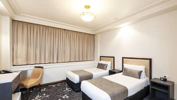 A hotel room with two beds, a desk, a chair, a nightstand, and a large window with curtains.