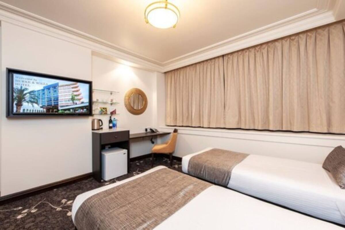 A hotel room with two beds, a desk, a chair, a television, and a window with curtains.