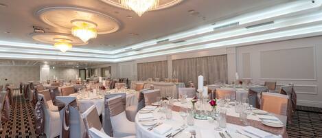 A banquet hall with round tables, white tablecloths, and elegant chandeliers.