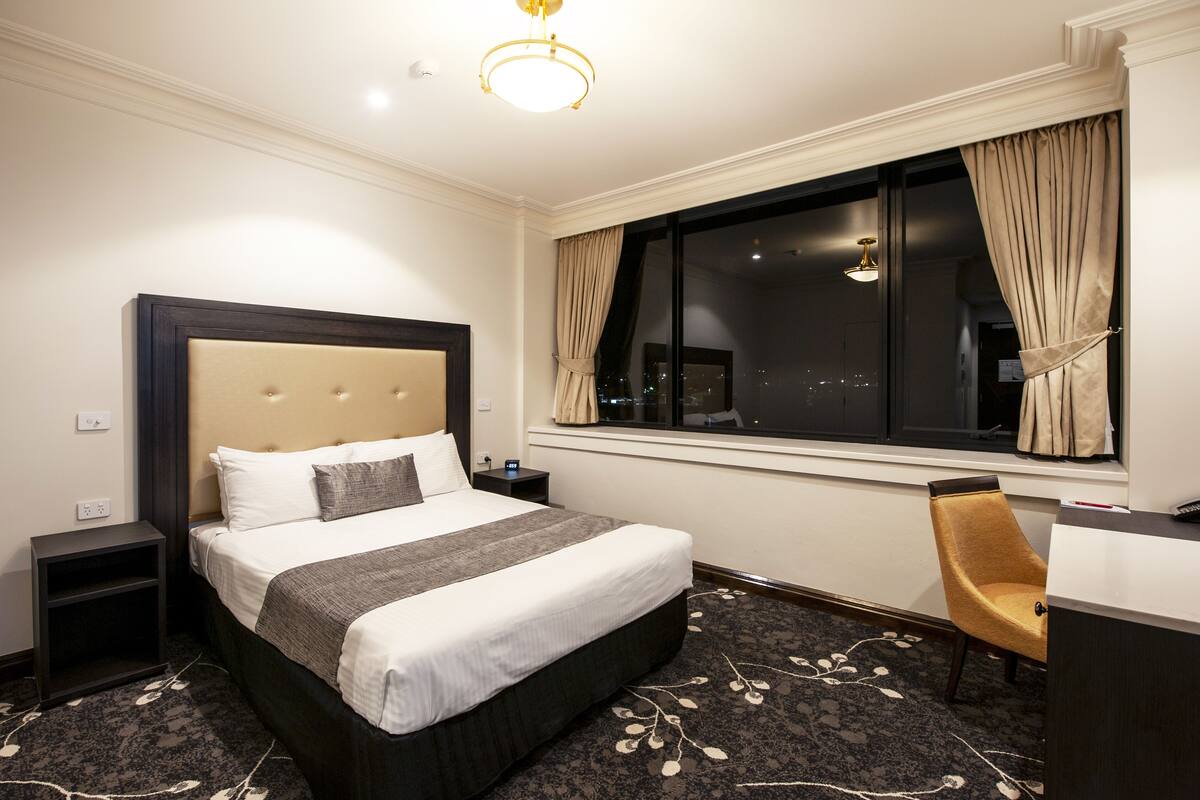 A hotel room with a large bed, a desk, and a chair.