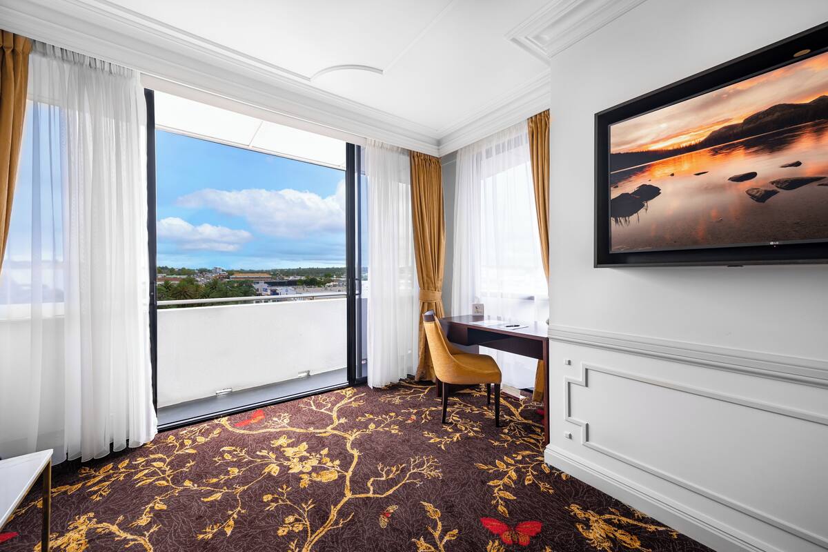 A hotel room with a large window, a desk, a chair, and a flat-screen TV.