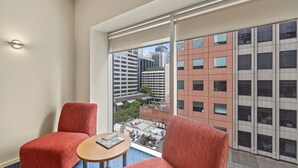 A hotel room with a large window, two red upholstered chairs, a small round table, and a view of city buildings. - YEHS Hotel Melbourne CBD (Melbourne)