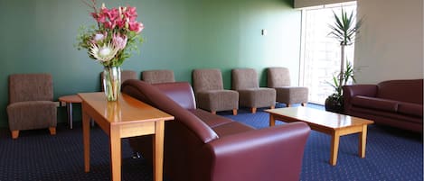 Un área de espera con un sofá marrón, una mesa de madera y un jarrón con flores.