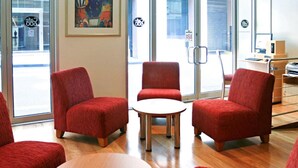A modern interior with red upholstered chairs, a round table, and a large window with a view of the street. - YEHS Hotel Melbourne CBD (Melbourne)