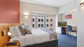 A hotel room with a bed, bedside table with a phone, a desk with a chair, a TV, and a window with a cityscape view. - YEHS Hotel Melbourne CBD (Melbourne)