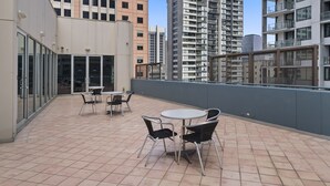A rooftop terrace with outdoor seating, large windows, and a view of surrounding high-rise buildings. - YEHS Hotel Melbourne CBD (Melbourne)