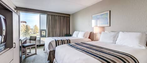 A hotel room with two beds, a desk, a chair, and a large window with curtains.