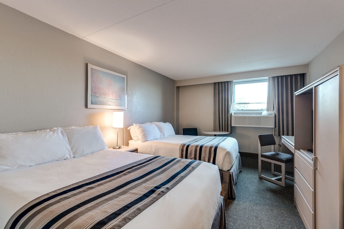 Une chambre d’hôtel avec deux lits, un bureau, une chaise, une fenêtre avec des rideaux et un tableau au mur.