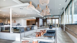 A modern hotel lobby with a seating area, wooden tables, and pendant lighting. - Heritage Inn Hotel & Convention Centre Saskatoon (Saskatoon)