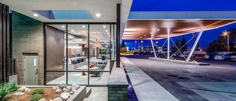A modern building with a glass facade, outdoor seating area, and a covered parking structure.