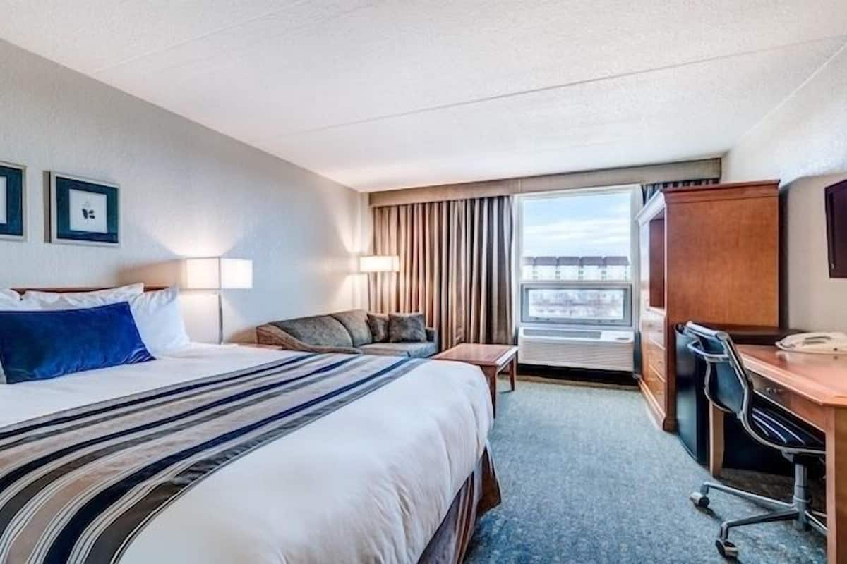 Une chambre d’hôtel avec un grand lit, un bureau, une chaise, une télévision et une fenêtre donnant sur un beau paysage.