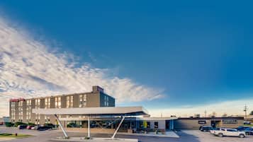 A hotel with a modern design, including a covered entrance and a parking lot with several cars.