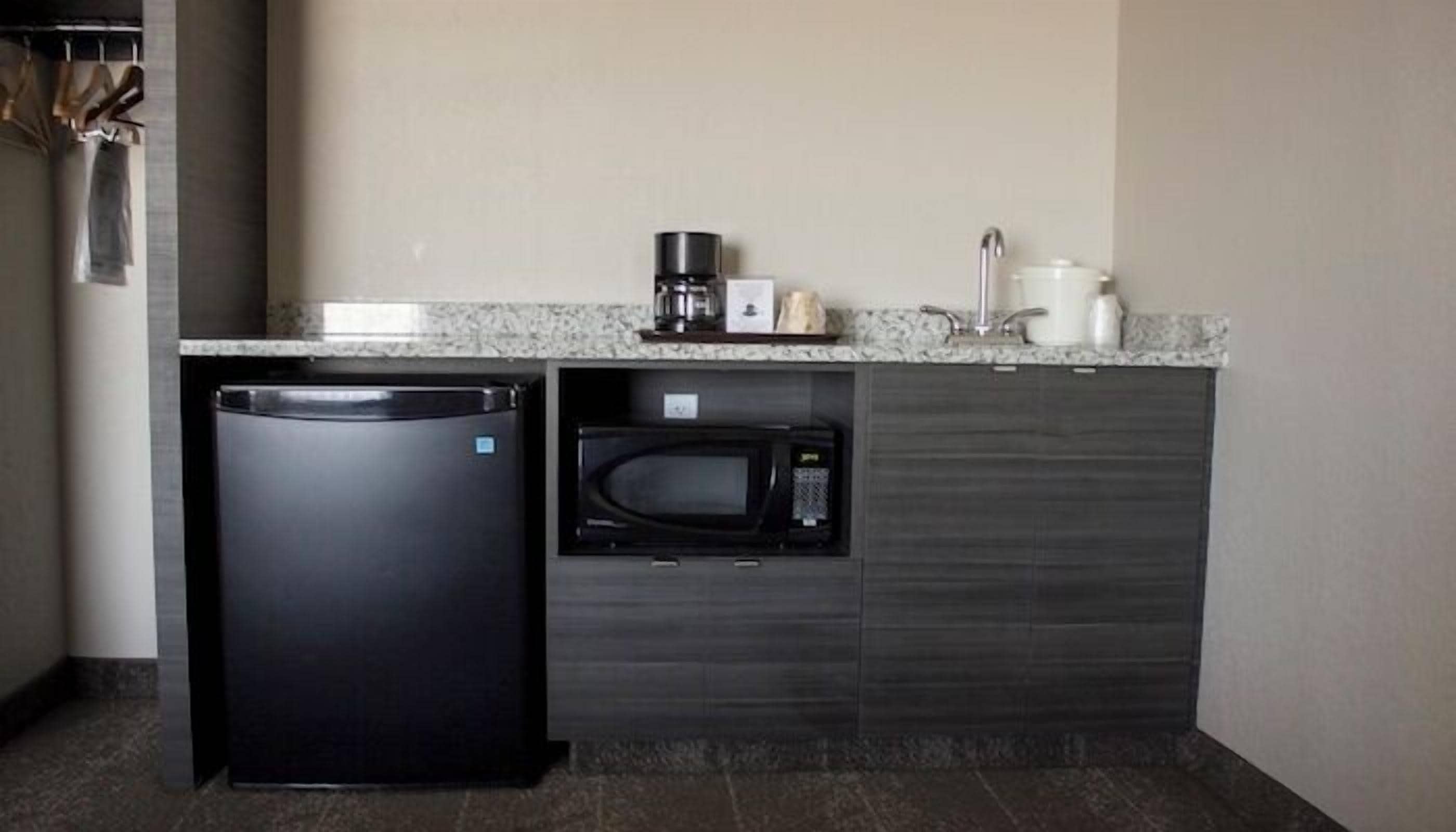 A compact kitchen with a refrigerator, microwave, coffee maker, and a sink.