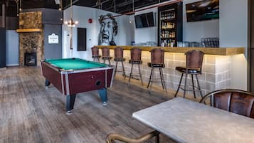 A billiards table, bar area with stools, and a fireplace in a lounge setting.