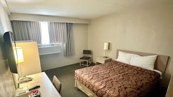 Une chambre d’hôtel avec un lit, un bureau doté d’une lampe, une chaise, une table de chevet et une fenêtre avec des rideaux.