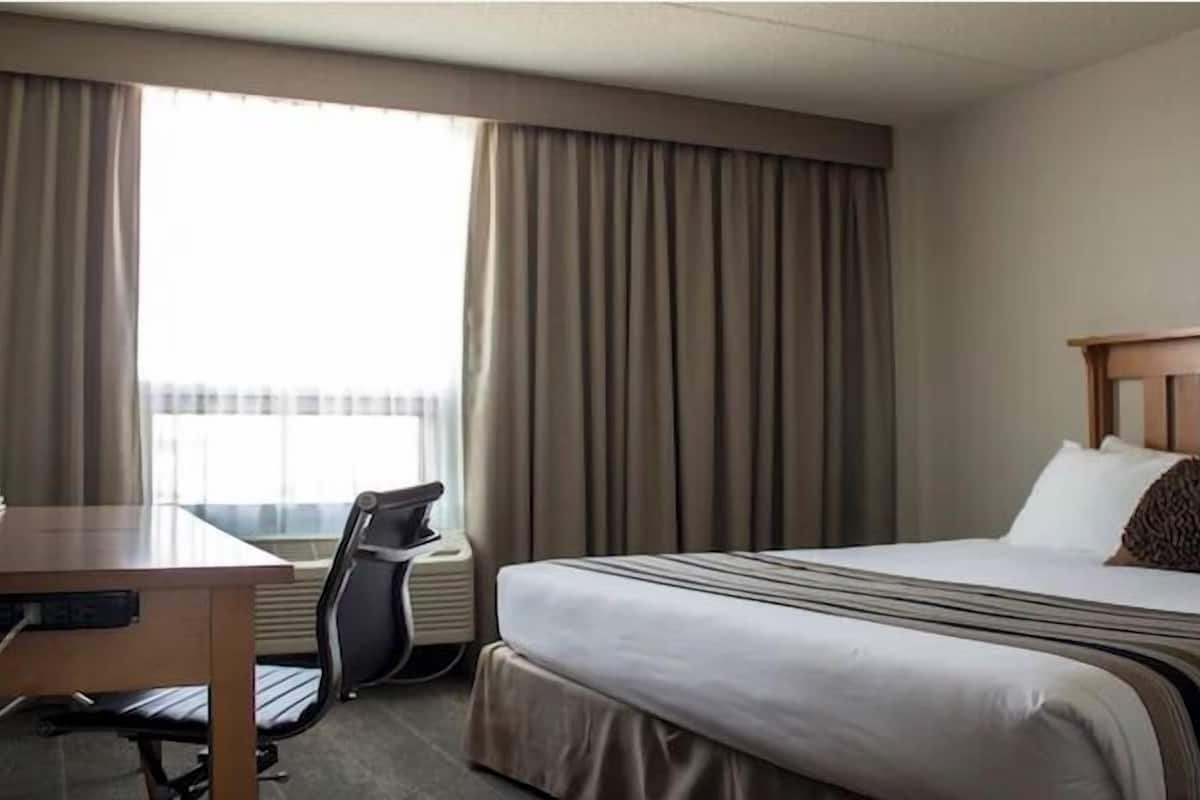 Une chambre d’hôtel avec un lit, un bureau, une chaise et une fenêtre avec des rideaux.