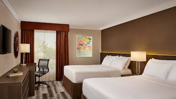 Habitación de hotel con dos camas, un escritorio, una silla, un televisor y un cuadro en la pared.