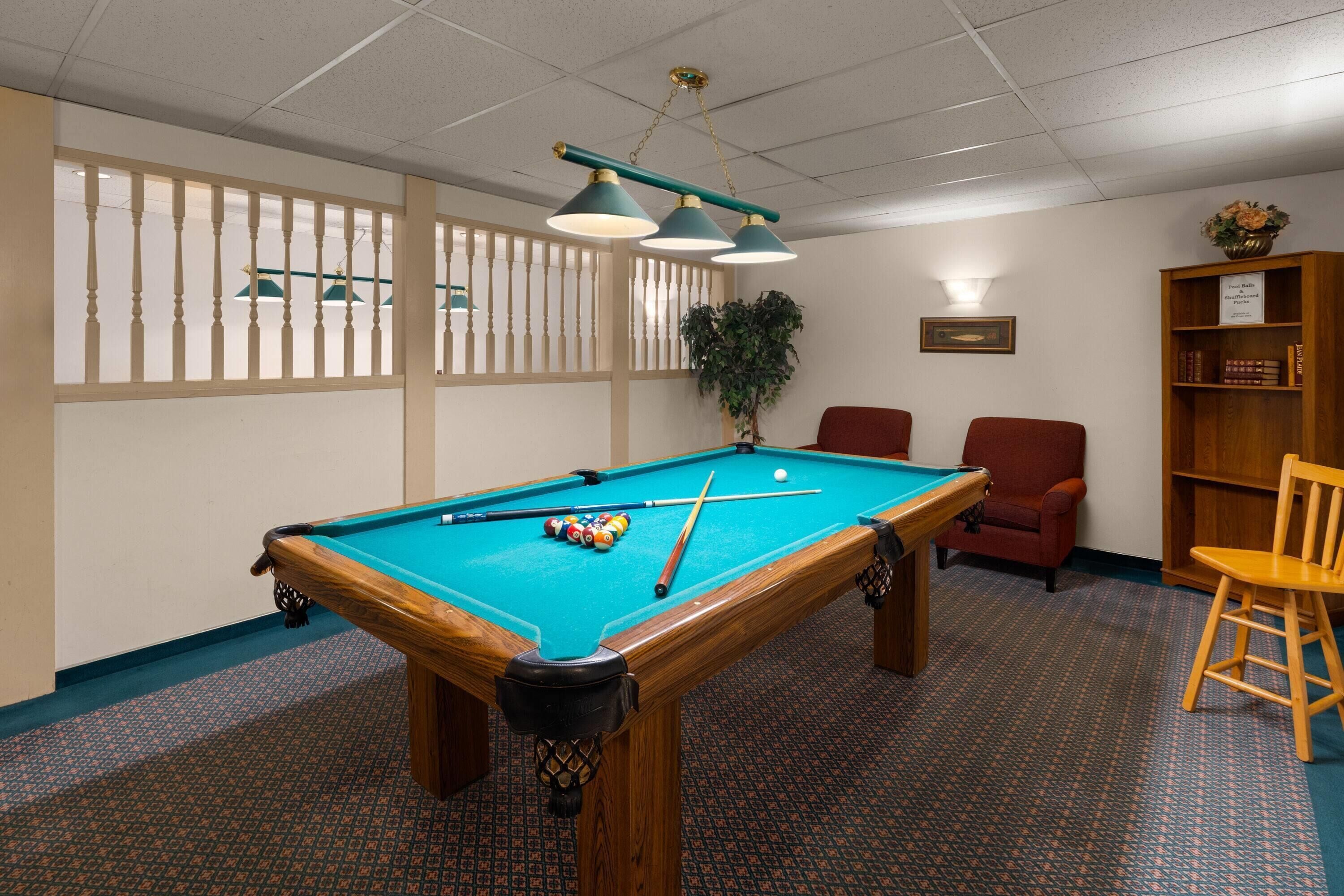A pool table with balls, a red chair, a wooden bookshelf, and a potted plant.