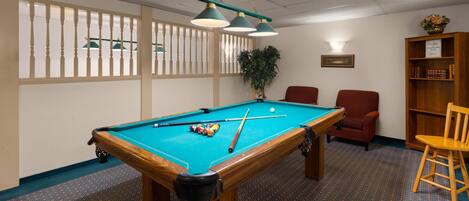 A pool table with balls, a red chair, a wooden bookshelf, and a potted plant.