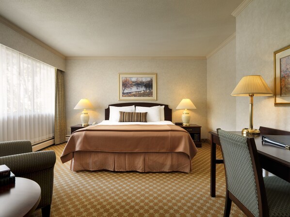 Una habitación de hotel con una cama grande, dos lámparas de noche, un escritorio, una silla y un ventanal con cortinas.