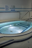 A swimming pool with steps and handrails, surrounded by tiled walls with safety instructions.