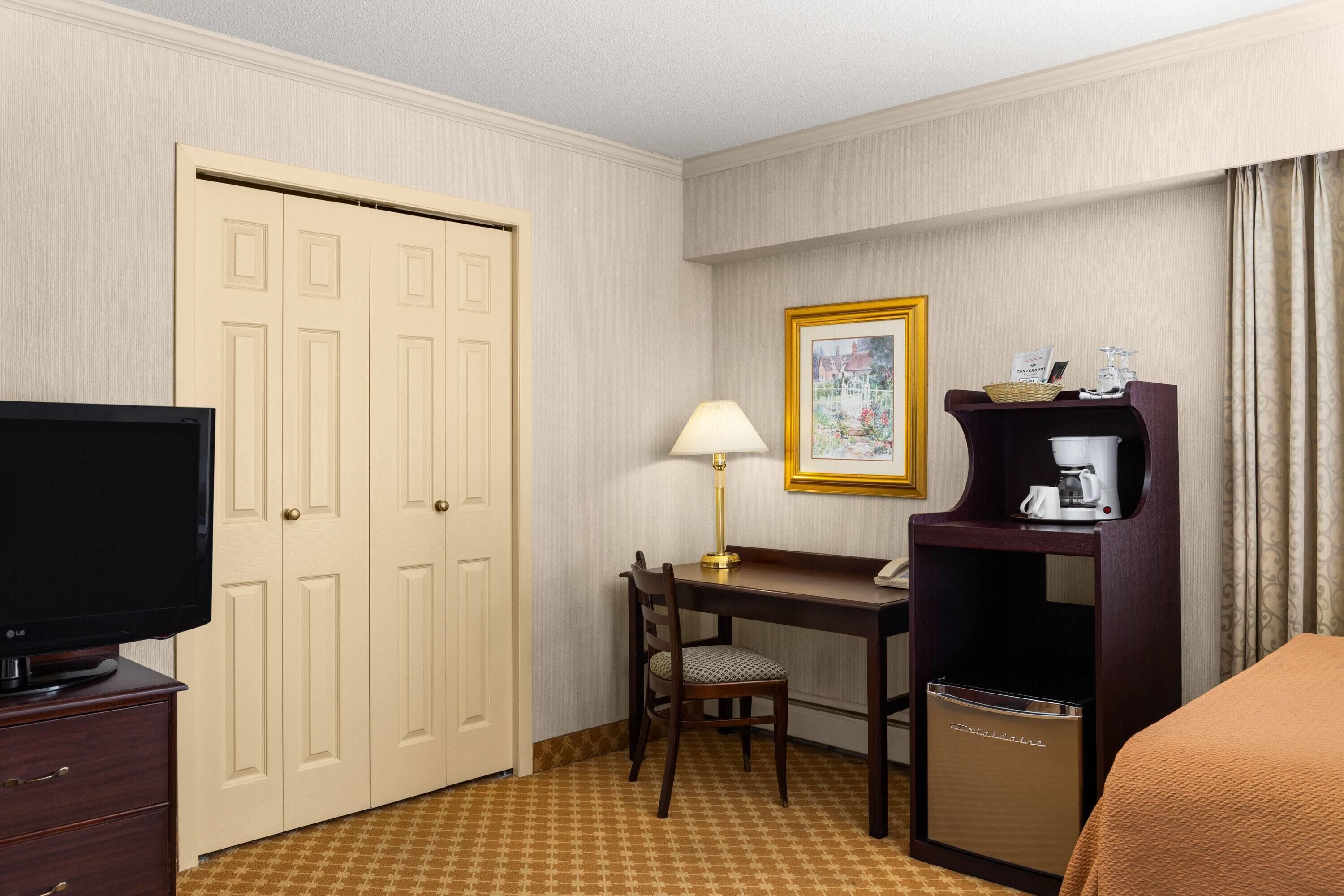 Habitación de hotel con televisor, escritorio con lámpara, silla, cafetera y cama.
