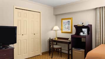 Habitación de hotel con televisor, escritorio con lámpara, silla, cafetera y cama.