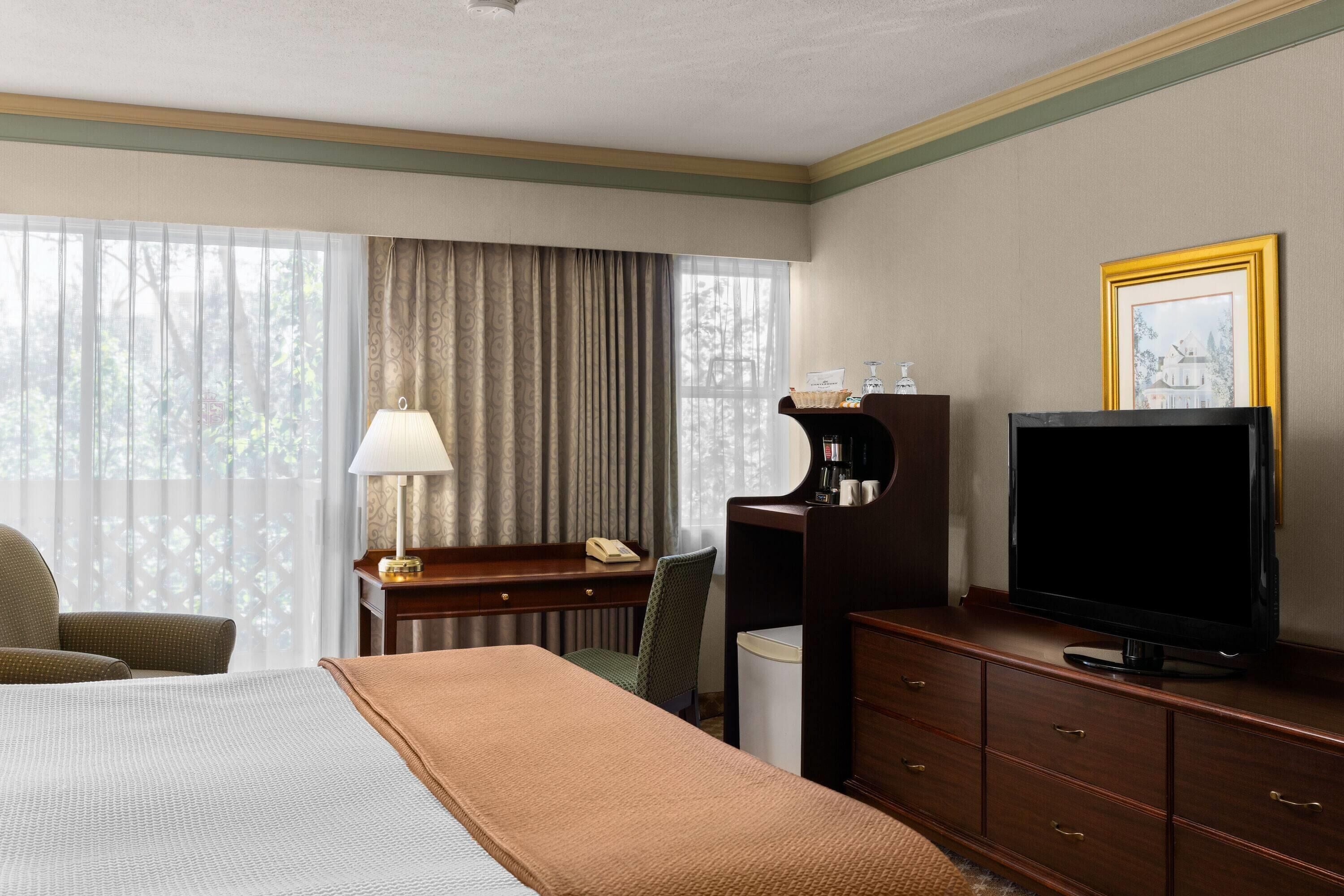 Quarto de hotel com uma cama, escrivaninha com luminária, televisão e cómoda.