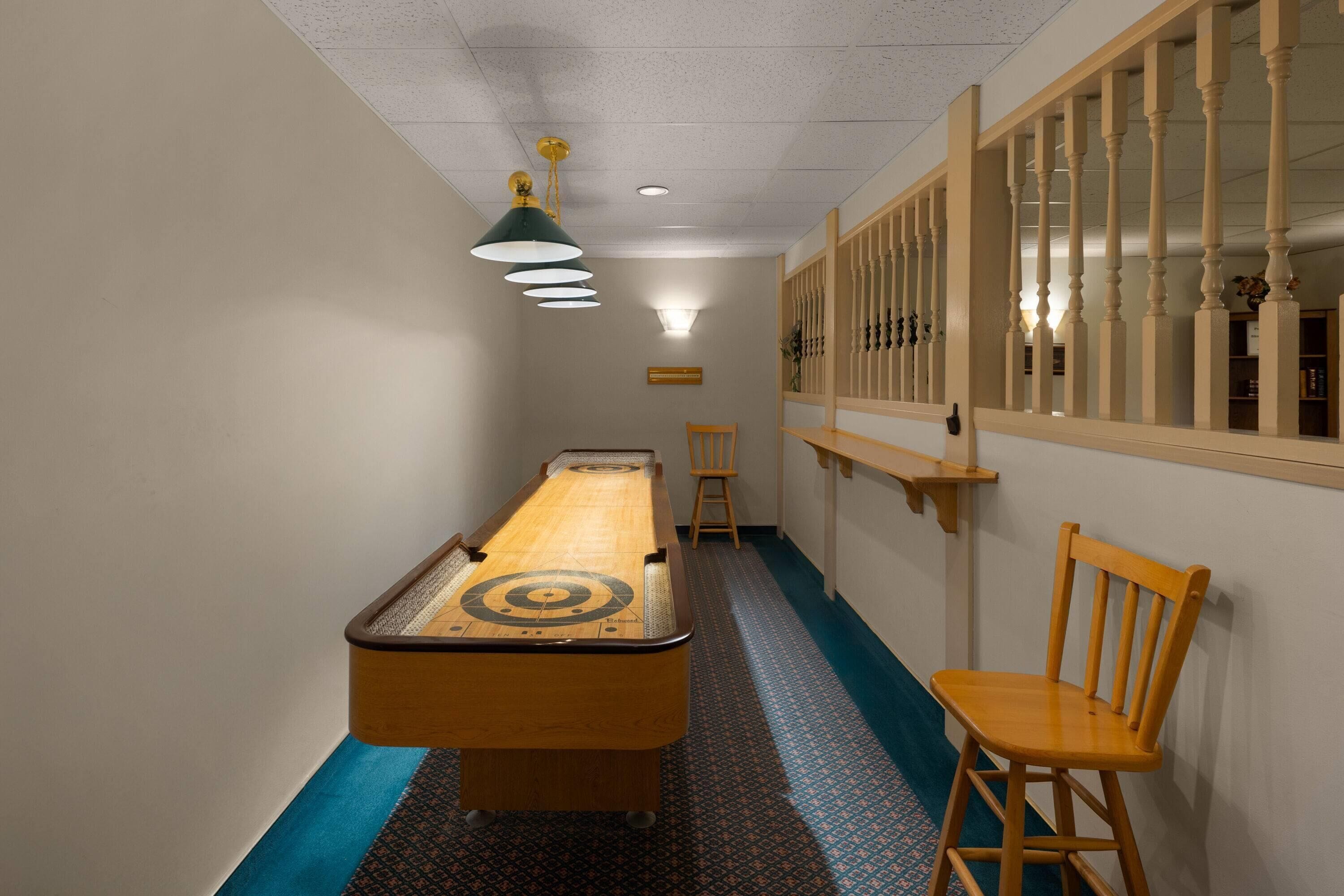 A narrow hallway with a pool table, a wooden chair, and a window with a wooden railing.