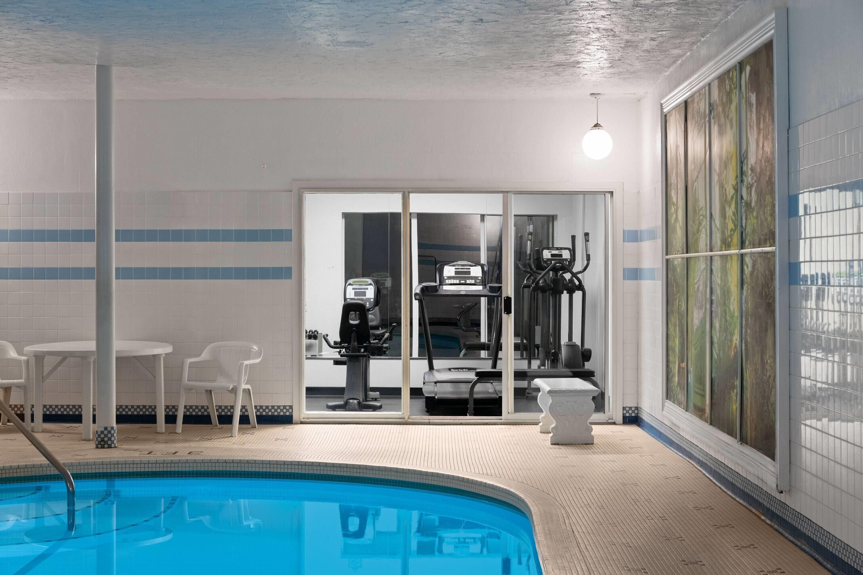 An indoor swimming pool with exercise equipment, a seating area, and a view through a glass door.