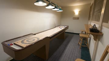 Uma mesa de bilhar com três luminárias suspensas, área de bar com banquetas e um tapete estampado.