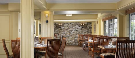 A dining area with wooden chairs and tables, a stone wall, and a patterned carpet.