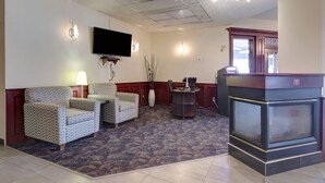 Vestíbulo de hotel con televisor de pantalla plana, dos sillones estampados, una mesa de centro, chimenea y mostrador de recepción.