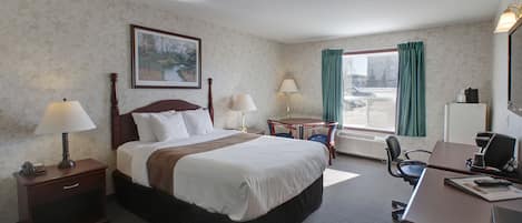 A hotel room with a large bed, two bedside tables with lamps, a desk with a computer, a chair, and a window with curtains.