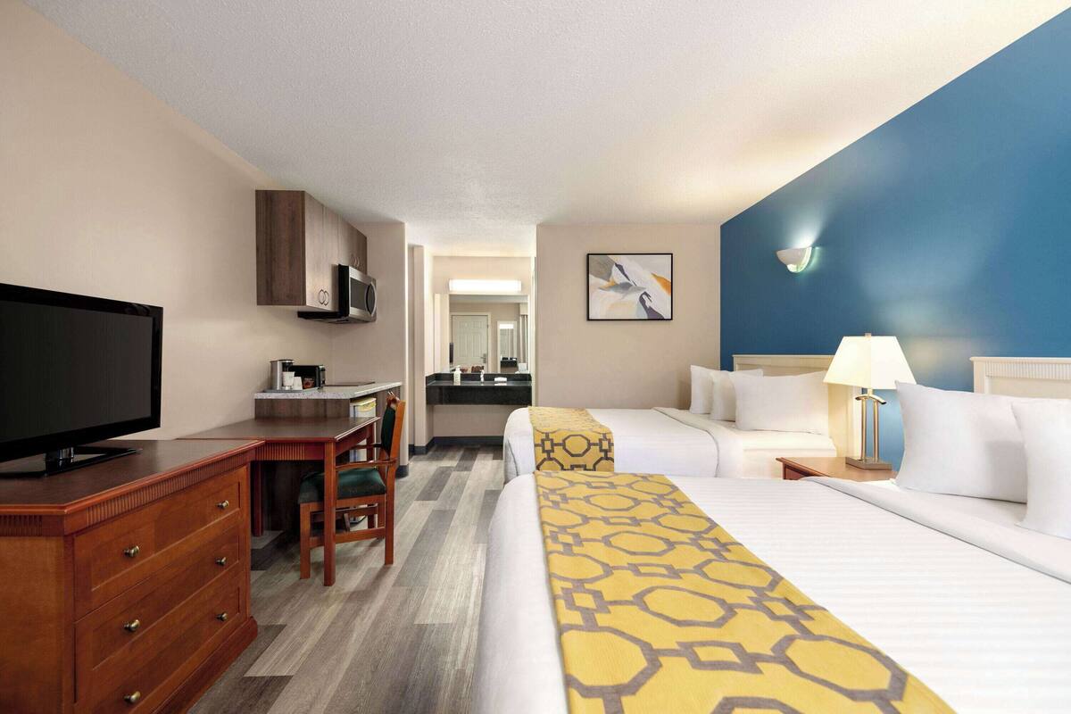 Une chambre d’hôtel comprenant un lit, un bureau avec une télévision, une chaise, une salle de bain et un tableau au mur.