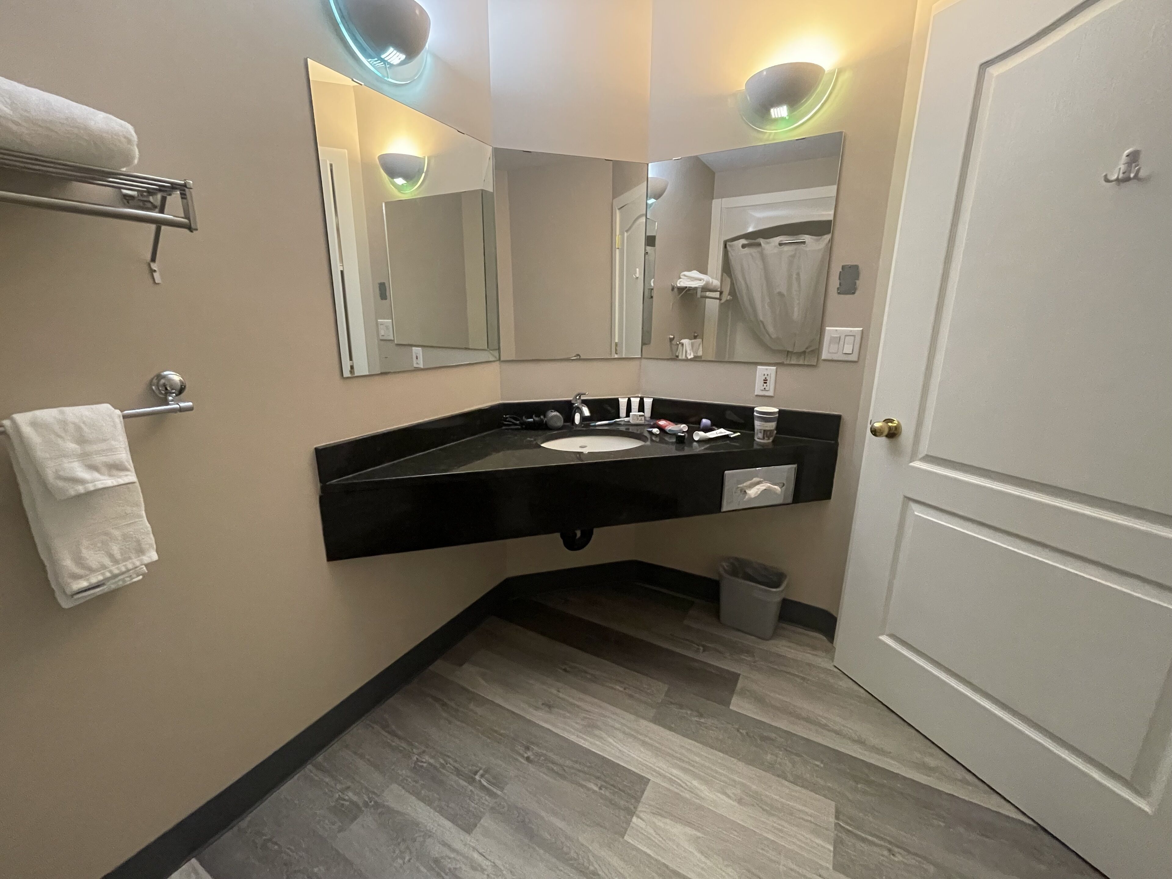 Une salle de bain avec un lavabo au comptoir noir, un miroir, un porte-serviettes et une porte.