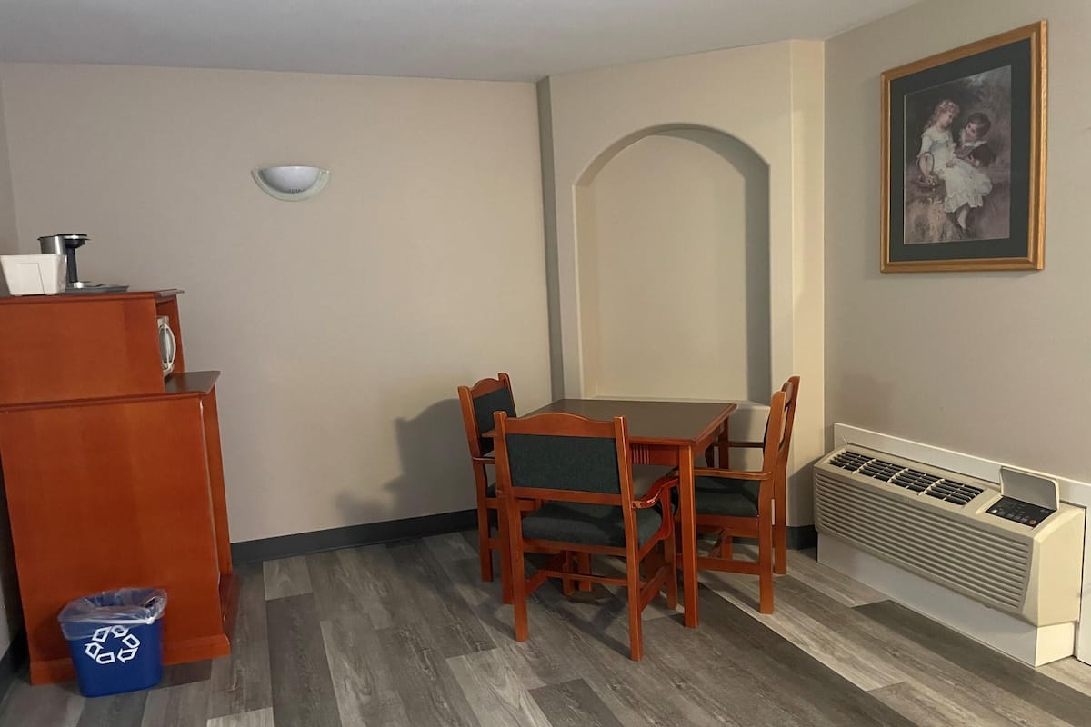 Un área de comedor con una mesa y sillas, un refrigerador pequeño, un cesto de basura, una lámpara de pared, un radiador y un cuadro enmarcado.