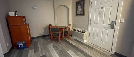 Una habitación con una mesa de comedor y sillas, un armario de madera, un radiador y una puerta con un letrero.