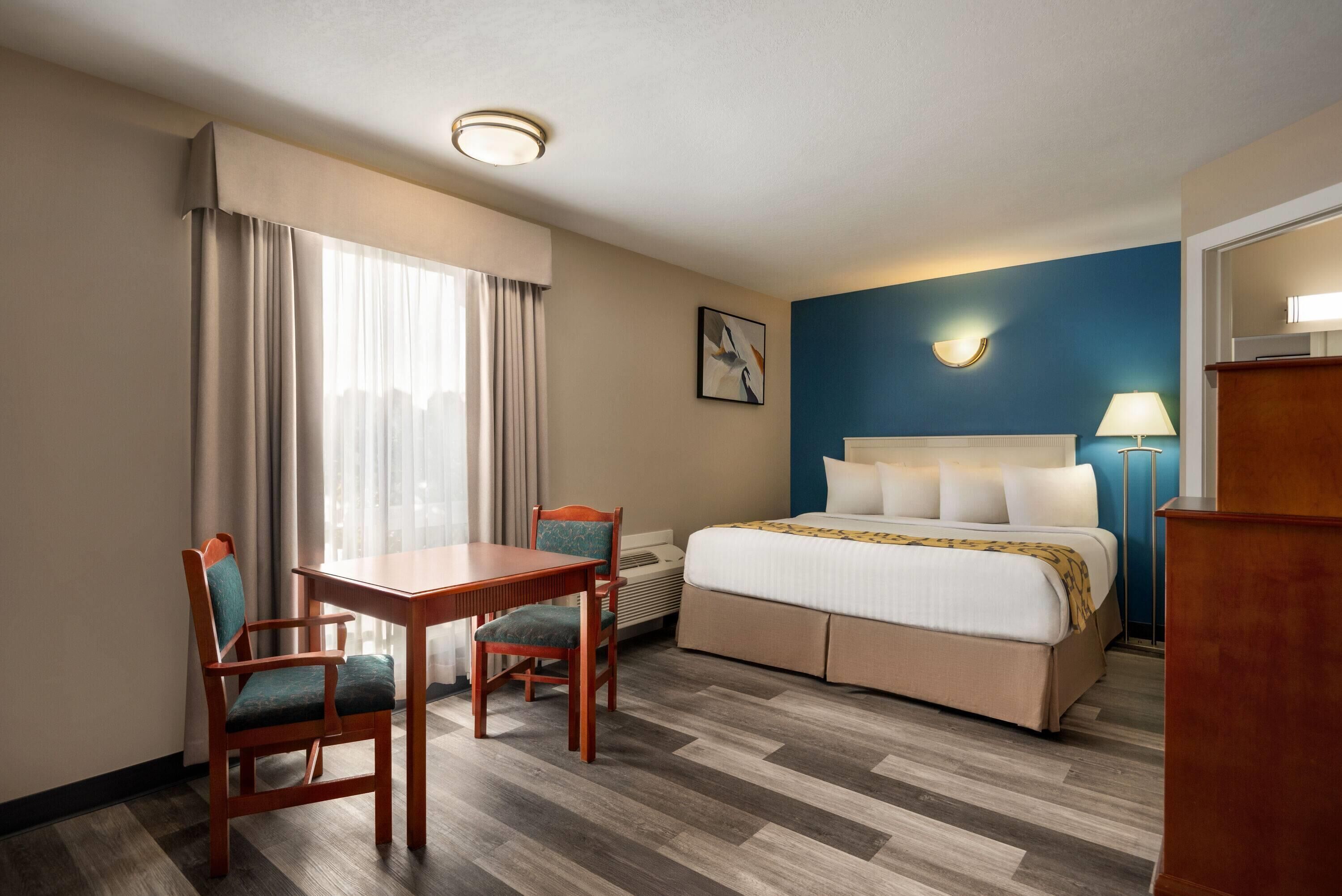 Hotellihuone, jossa on sänky, työpöytä, kaksi tuolia, lamppu ja taulu seinällä.