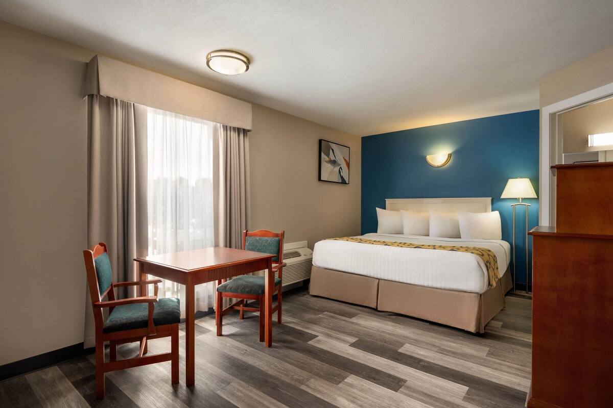 Une chambre d’hôtel avec un lit, un bureau, deux chaises, une lampe et un tableau au mur.