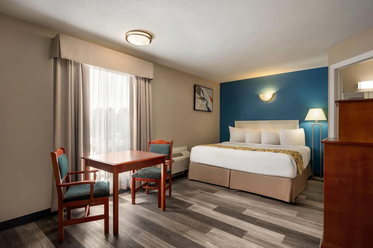 Habitación de hotel con cama, escritorio, dos sillas, lámpara y un cuadro en la pared.